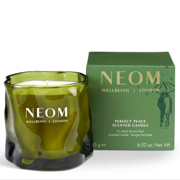An olive green glass scented candle with a wick and white wax, shown next to its matching green packaging box. The brand NEOM is clearly visible on both the candle and the box.