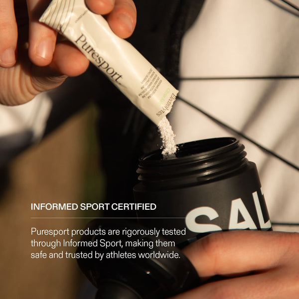 Person pouring a electrolytes powder from a Puresport sachet into a black sports bottle with a informed sport certified badge. 