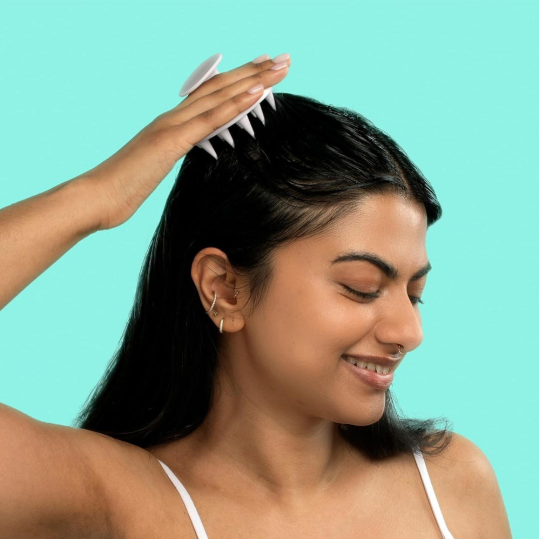 Woman using a hair product on her hair against a teal background