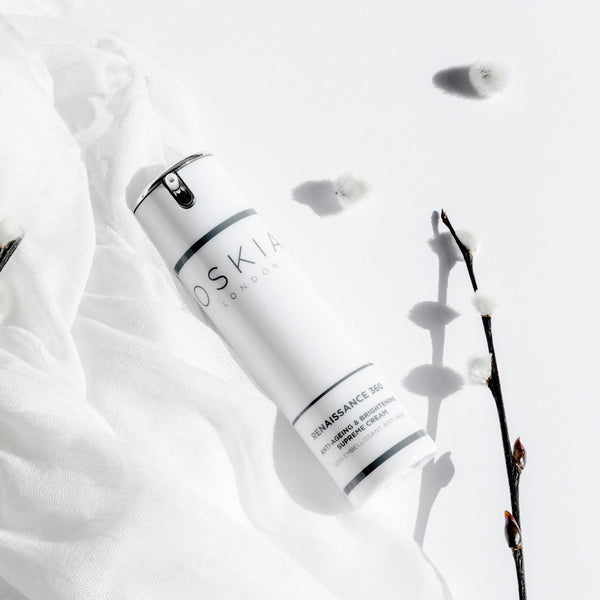 OSKIA Renaissance 360 Anti-Ageing and Brightening Supreme Cream Travel bottle on a while cloth with a cotton branch laid next to it