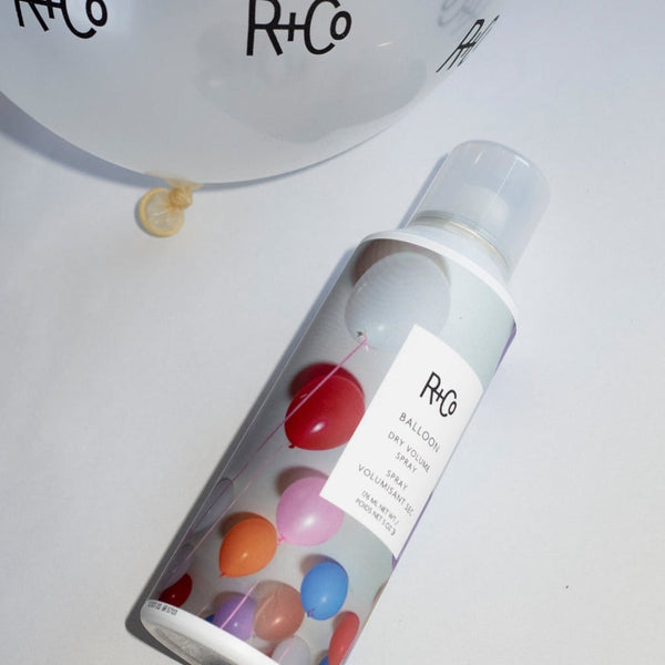 a bottle of R+Co Balloon Dry Volume Spray next to an R+Co Balloon