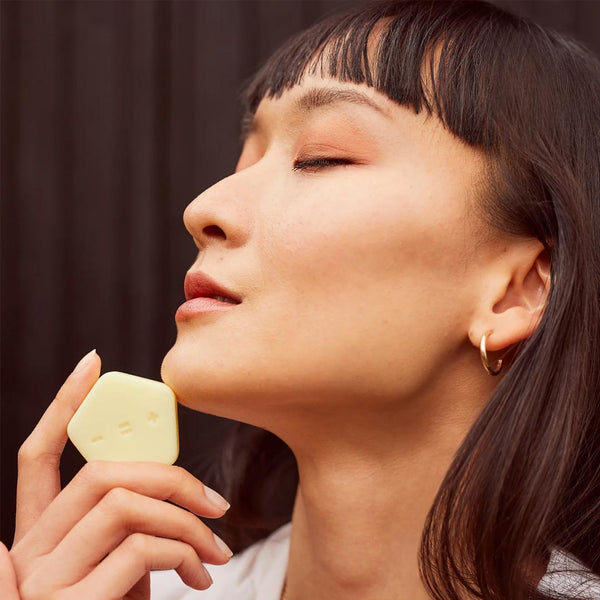 a woman holding a bar of SBTRCT Rejuvenating Night Balm to her chin