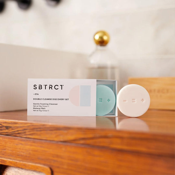 SBTRCT The Double Cleanse Discovery Set on a wooden counter in a bathroom setting