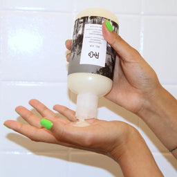 a bottle of R+Co Bel Air Smoothing Shampoo being squeezed into a hand