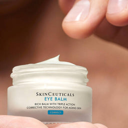 a hand dipping their fingers into a tub of SkinCeuticals Eye Balm