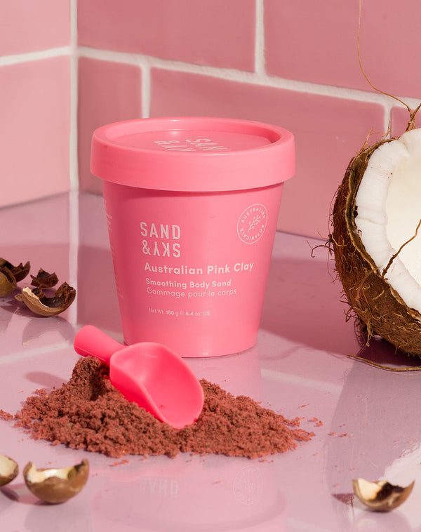 Sand & Sky Australian Pink Clay Smoothing Body Sand Bucket on a counter top with a scoop and coconut 
