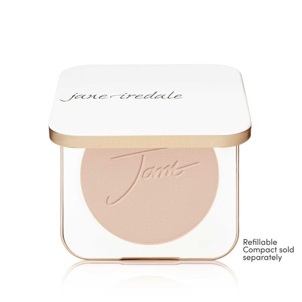 A Jane Iredale makeup compact with a white lid and a clear base showing a round blush or pressed powder in a light peach-beige shade. The compact has a thin metallic gold frame.