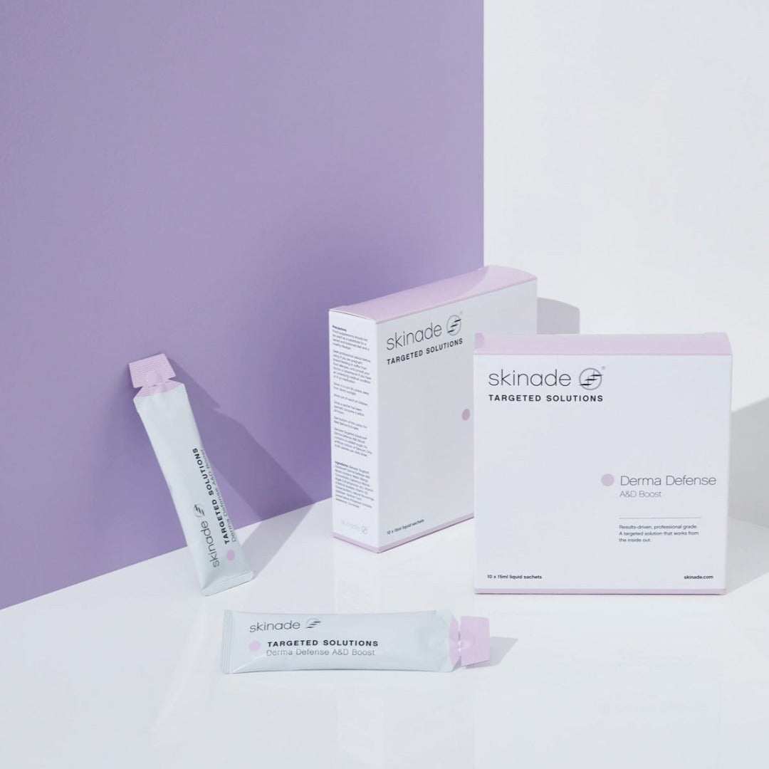 two packets of Skinade Targeted Solutions Derma Defense A and D Boost in front of a purple wall
