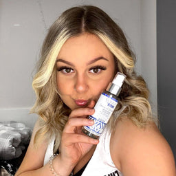 a woman holding a bottle of Skinny Tan Coconut Water Bronzing Face Mist close to her face