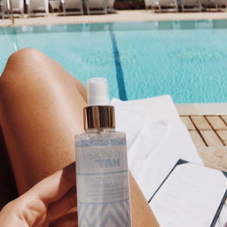 a bottle of Skinny Tan Coconut Water Tanning Mist held by the side of a pool