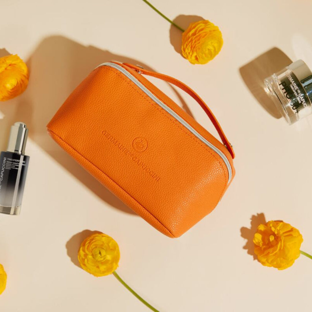 Orange cosmetic bag with a brand logo surrounded by yellow flowers on a light background