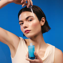 Woman applying skincare product with dropper against a blue background