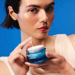 Woman holding a blue skincare jar against a blue background
