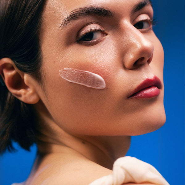 Woman applying cream to her face with a blue background