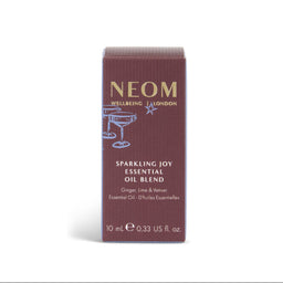 A tall rectangular box of NEOM Wellbeing London Sparkling Joy Essential Oil Blend, featuring a deep burgundy-brown color with gold and light blue text and illustrations, set against a plain white background.