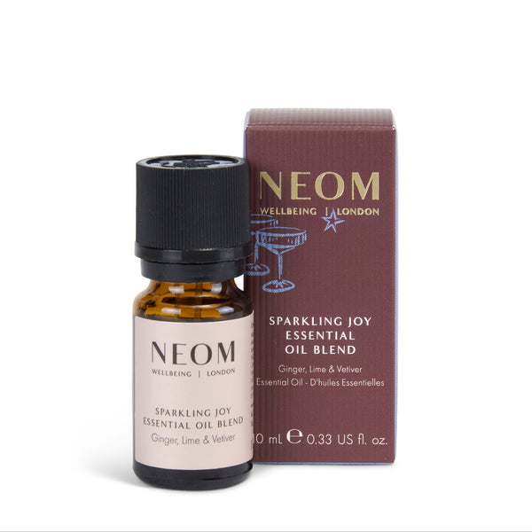 NEOM Wellbeing London Sparkling Joy Essential Oil Blend in a 10 mL amber glass bottle with a black cap, shown next to its dark burgundy box on a white background.