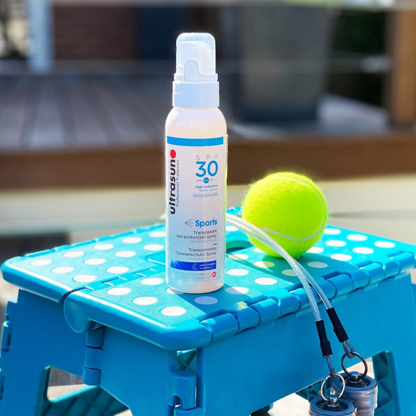 White Ultrasun Sports Spray SPF 30 150ml bottle on blue step next to tennis ball