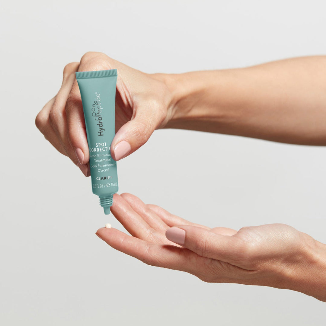 Hand holding a tube of skincare product against a neutral background
