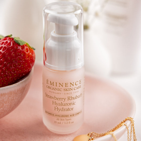 Eminence skincare product with strawberry and gold necklace on a light background
