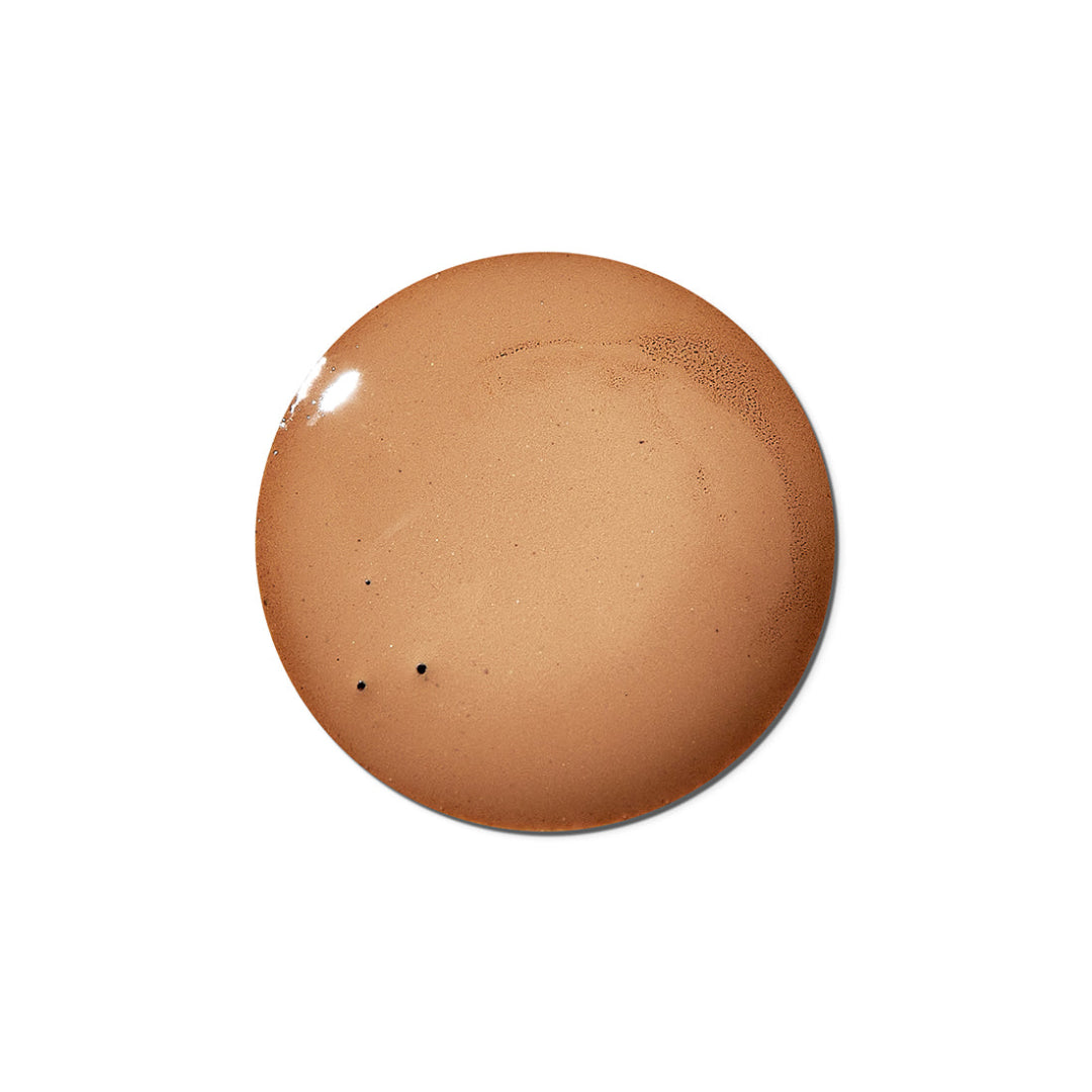 A circular swatch of warm tan-brown cosmetic cream or liquid foundation on a plain white background.