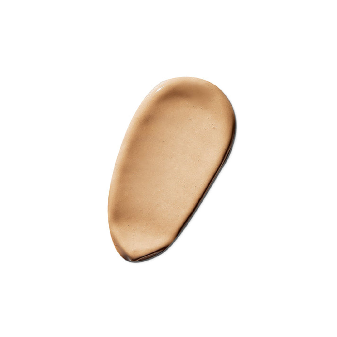 A smooth, teardrop-shaped smear of liquid foundation in a warm tan shade, centered on a solid white background.