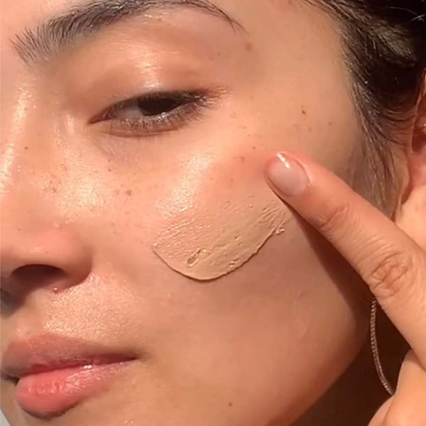 a closeup of a woman applying PRIORI TETRA Broad Spectrum SPF 55 with Universal Skin Tint to her face