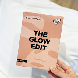 A hand holding a Beautypro 'The Glow Edit' SPA at home box against a soft white background.
