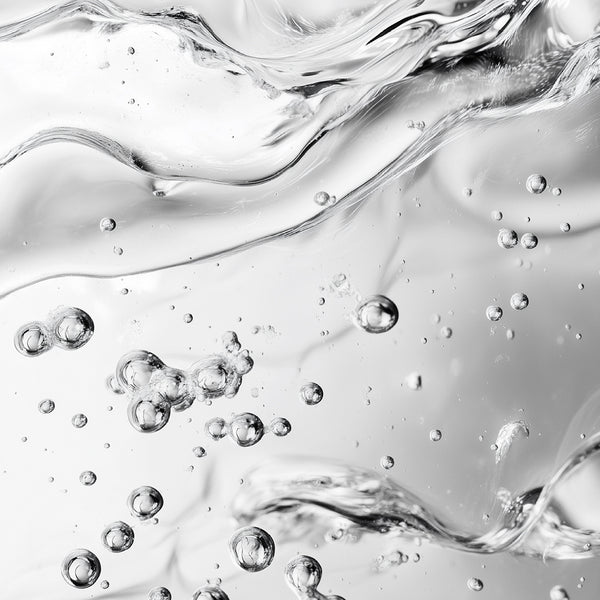 Abstract close-up of clear liquid with flowing ripples and scattered transparent bubbles in a monochrome gray-white composition.