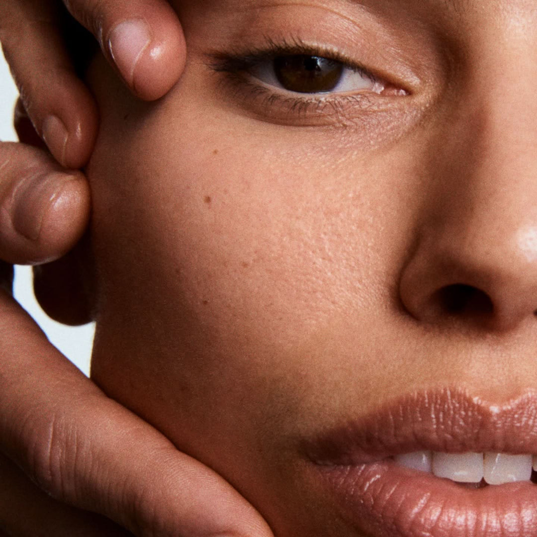 Extreme close-up of a person's face showing clear skin texture, with fingers gently holding the cheek and jaw area.