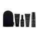 A set of five black haircare products from Three Warriors, including a towel, shampoo, conditioner, hair oil, and hair mask, arranged on a plain white background.