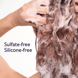 Close-up of a person washing long brown hair with thick white foam, with text reading 'Sulfate-free Silicone-free' on a white background.