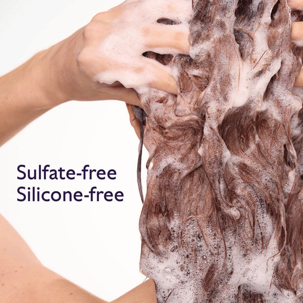 Close-up of a person washing long brown hair with thick white foam, with text reading 'Sulfate-free Silicone-free' on a white background.