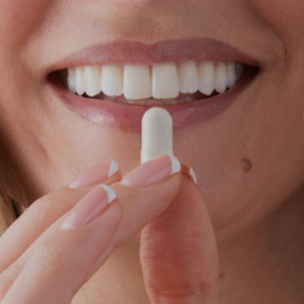 Close-up of a smiling woman holding a white tablet near her mouth, with text reading 'Iron, supercharged' and additional supplement benefit copy on a light background.