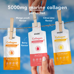 Three Zooki collagen supplement sachets hang from a rope with wooden clothespins against a blue sky background. A hand holds the center sachet, and text labels the flavors: Mango Peach, Berry, and Citrus Lime.