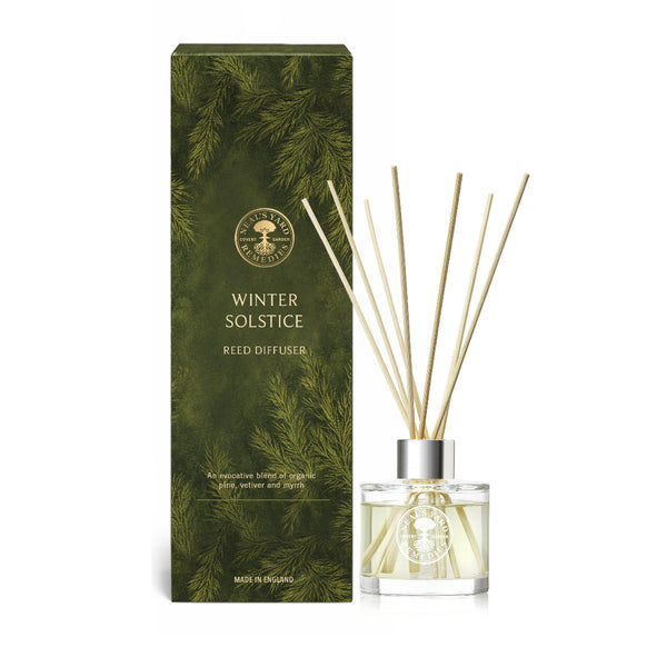 Winter Solstice Reed Diffuser by Aromatic Rooms, featuring a dark green pine-patterned box next to a clear glass bottle filled with reed diffuser liquid and natural reed sticks, on a white background.