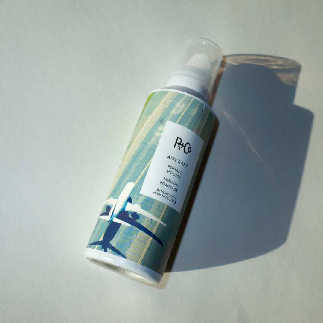 a closeup  of a R+Co Aircraft Pomade Mousse bottle