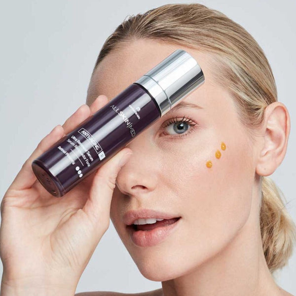 Model holding ALLSKIN MED R Ultra Renewal Serum with 3 dots of the serum on her cheek