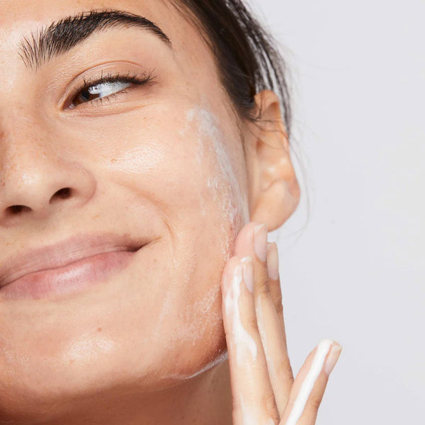 Woman applying a skincare product to her face with a neutral background
