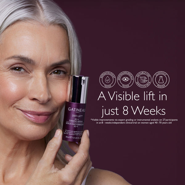A close-up of a smiling woman with silver-gray hair holding a bottle of Gatineau DerLift+ facial moisturizing serum against a dark plum background, with text and certification icons on the right.