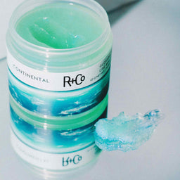 a tub of R+Co Continental Glossing Wax with a smudge of texture on a mirror 