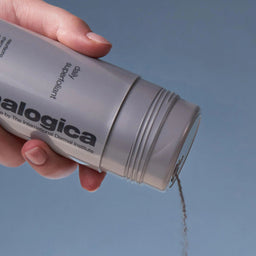 Hand holding a skincare product labeled 'alogica' against a blue background