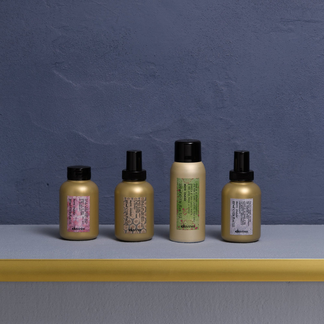 Four gold-colored hair care products with black caps on a gray surface against a blue wall.