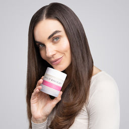 Woman holding a Philip Kingsley skincare product against a gray background
