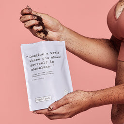 Cacao coffee scrub packaging held by a hand with a pink background