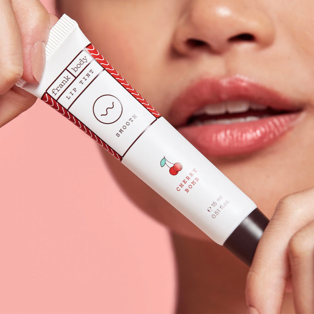 Lip balm with cherry flavor packaging held by a person against a pink background