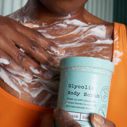 Person using Glycolic Body Scrub on their arm with a container of the product in hand.