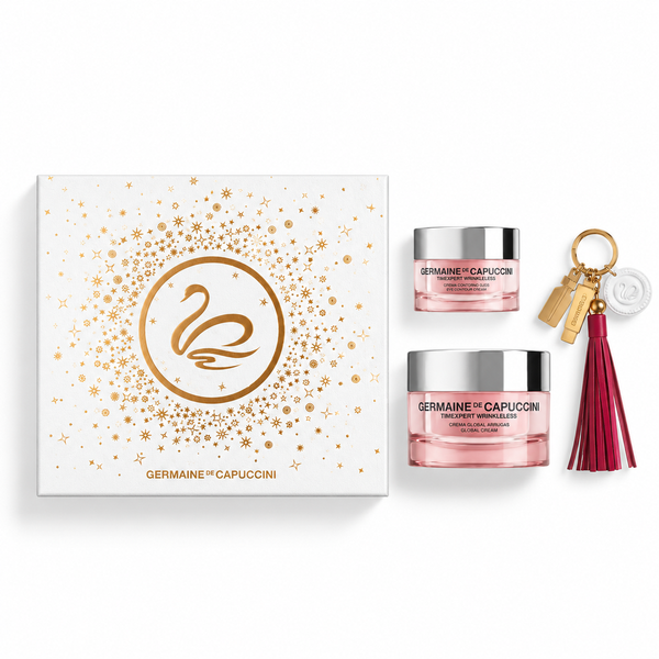 A Germaine Capuccini gift set on a white background, featuring a white box with gold swan and starburst graphics, two pink treatment creams in silver jars, and a gold keychain with a burgundy tassel.