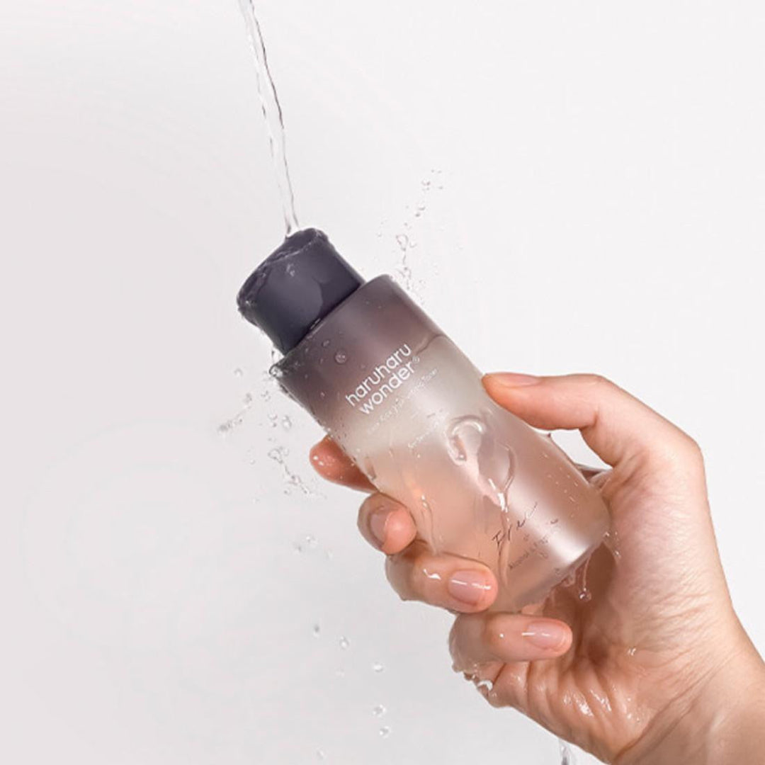 Hand holding a clear bottle with a dark cap, labeled 'haruharu wonder', against a light background.