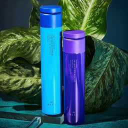 two bottles of R+Co Bleu in front of a large plant