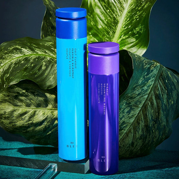 two bottles of R+Co Bleu in front of a large plant
